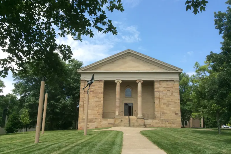 Rosse Hall at Kenyon College in Gambier, Ohio, a sandstone hall with a columned porch at the end of a path across the lawn.