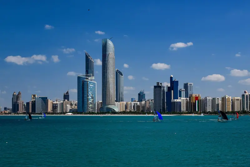 The Abu Dhabi skyline across the water, with small sailboats in the foreground.